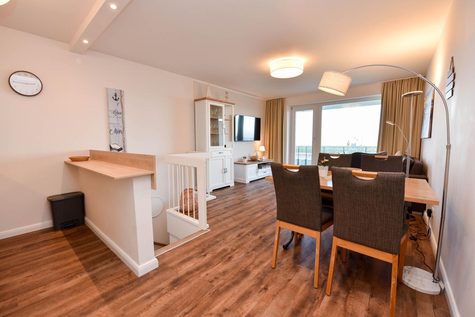 Wohn- und Essbereich mit Holzboden, Esstisch, TV und Balkontür.