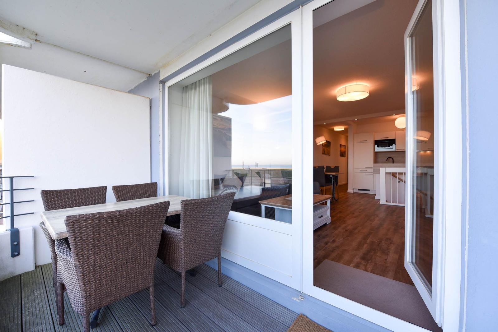 Terrasse mit Esstisch und Stühlen. Blick ins Innere mit Küche und Wohnbereich.