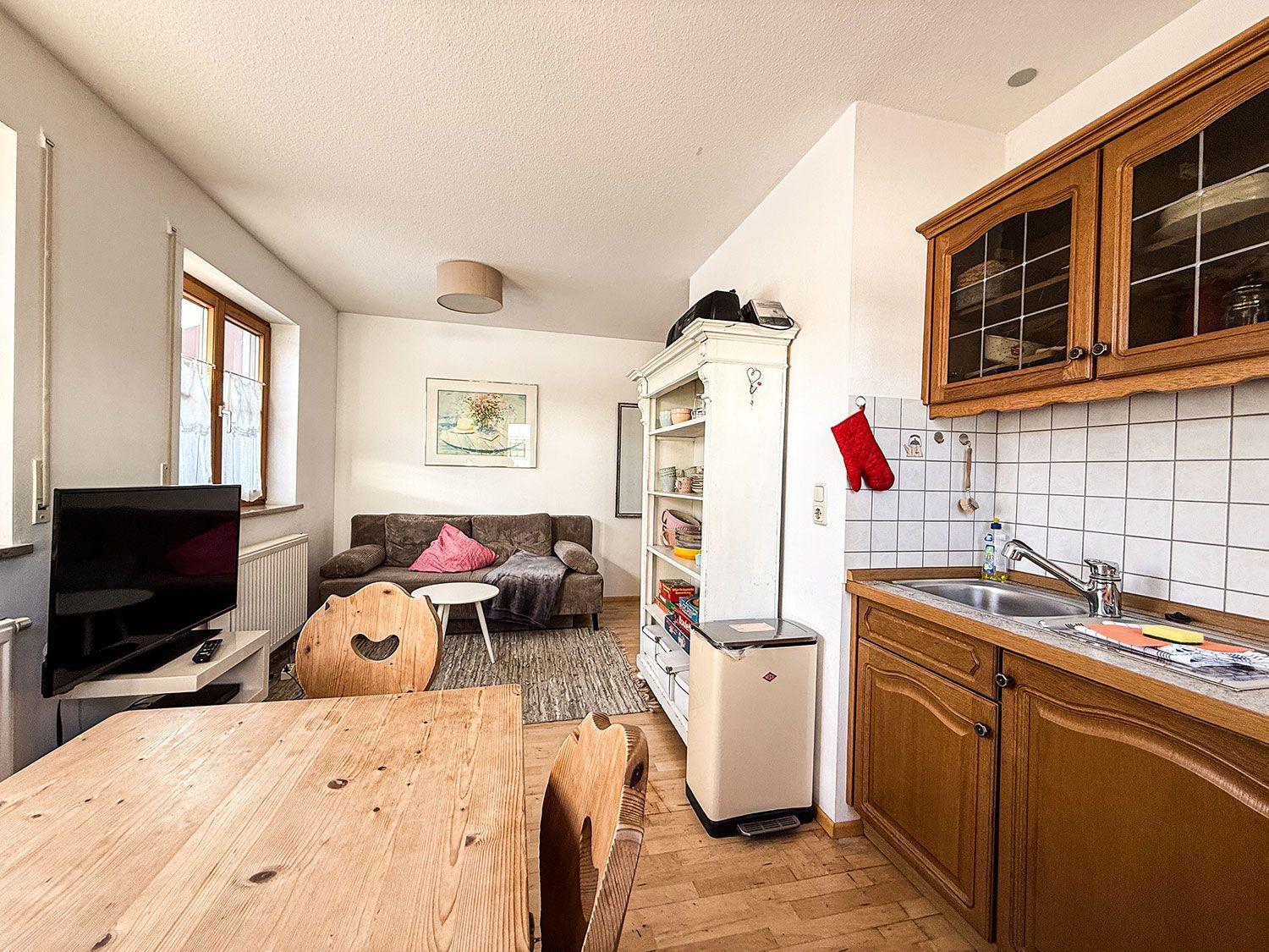 Küche mit Holzschränken, Esstisch, Sofa und Fernseher im Wohnbereich.