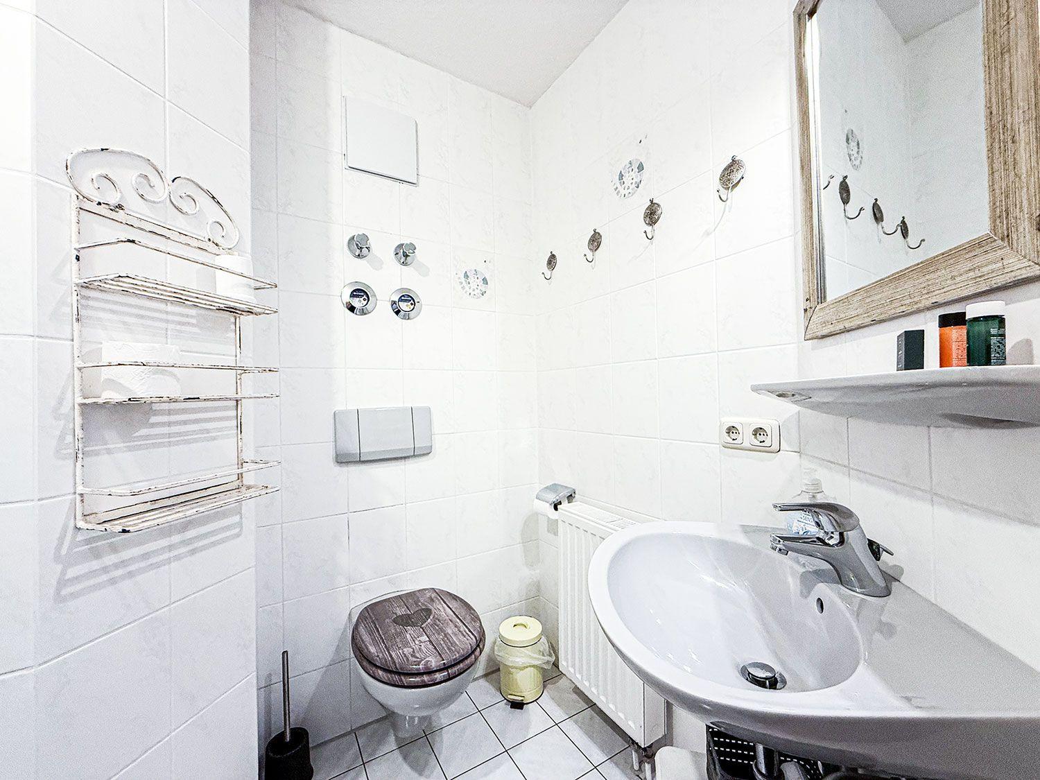 Badezimmer mit Waschbecken, Toilette und Dusche. Weiße Fliesen und Spiegel.