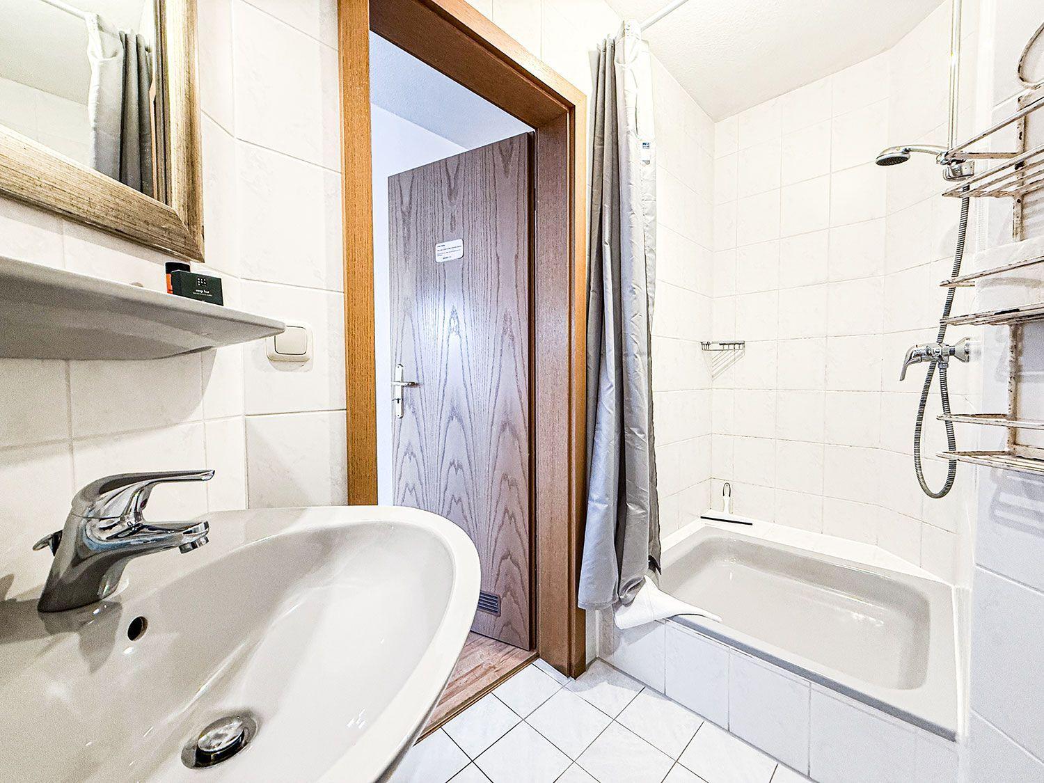 Badezimmer mit Badewanne, Duschkopf und Waschbecken mit Spiegel.