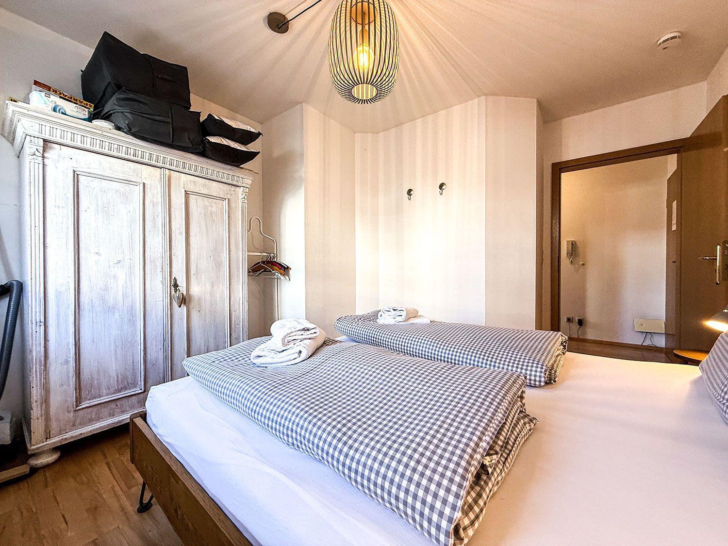 Zimmer mit Doppelbett, Kleiderschrank und Decken. Decke mit Lampe und Tür.