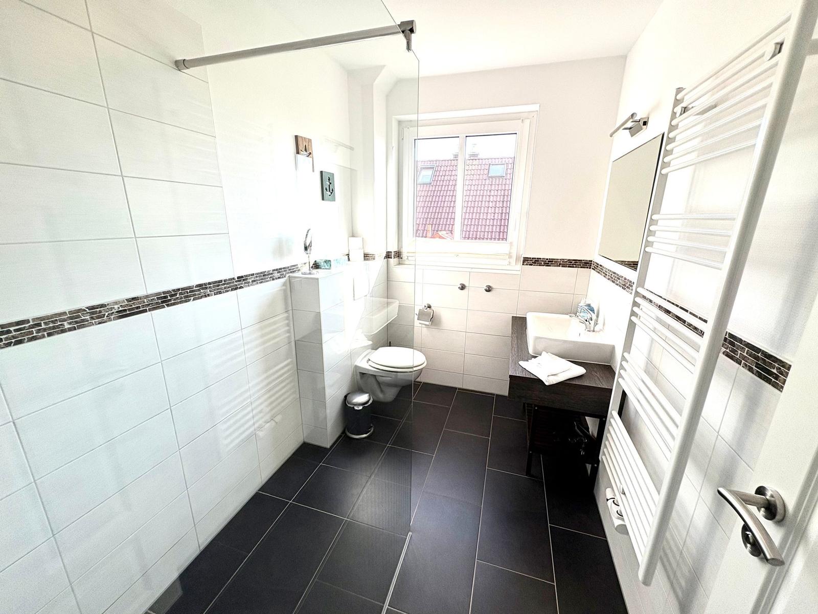 Badezimmer mit Dusche, Toilette, Waschbecken und Heizkörper.