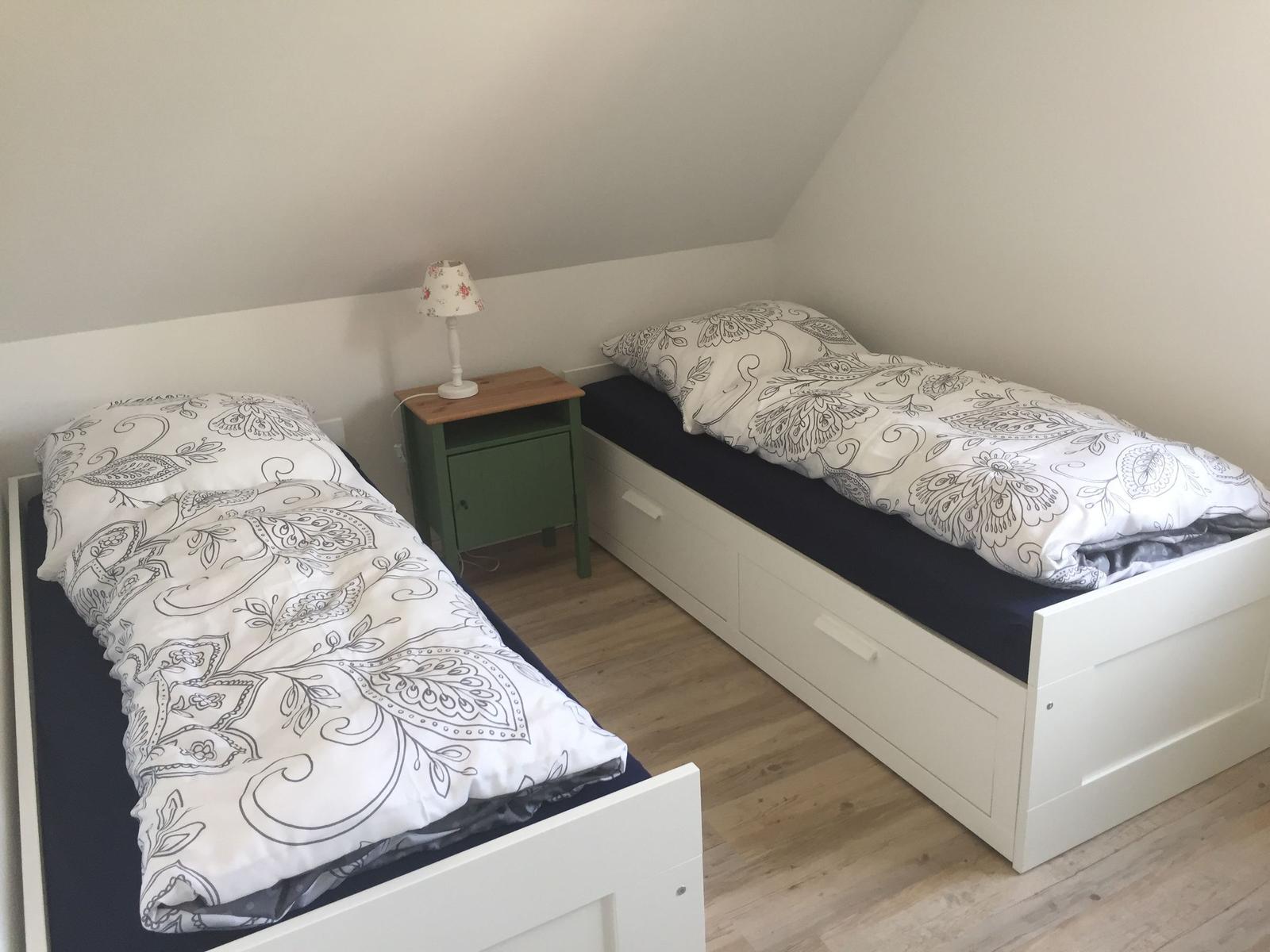 Zwei Einzelbetten mit Musterdecken und Nachttisch mit Lampe