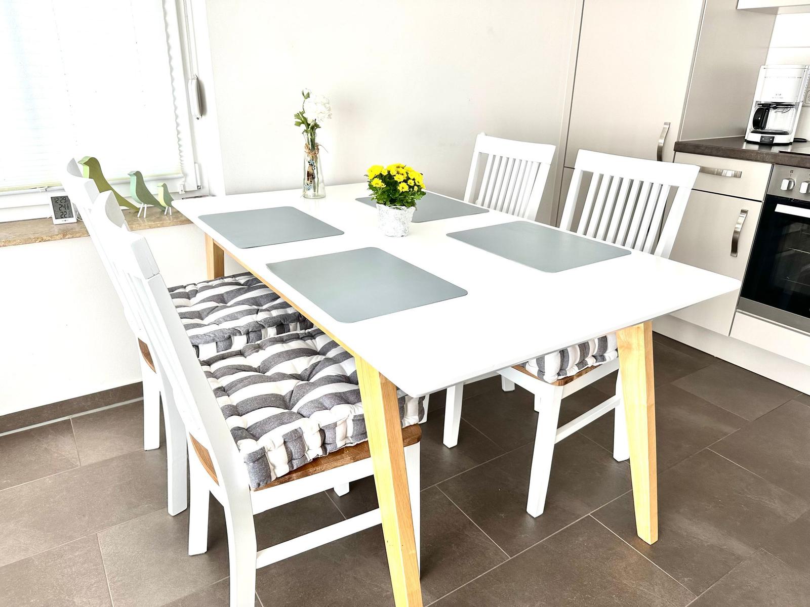 Essbereich mit weißem Tisch, vier Stühlen und Blumen.
