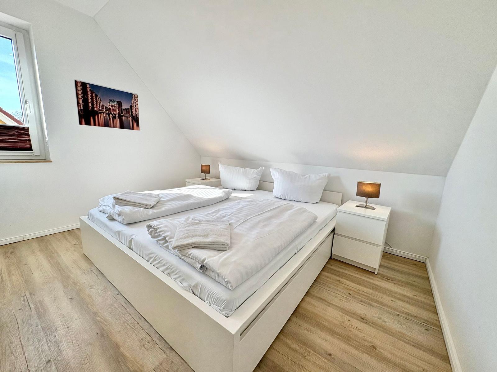 Schlafzimmer mit Dachschrägen, weißem Bett und Nachttischen.