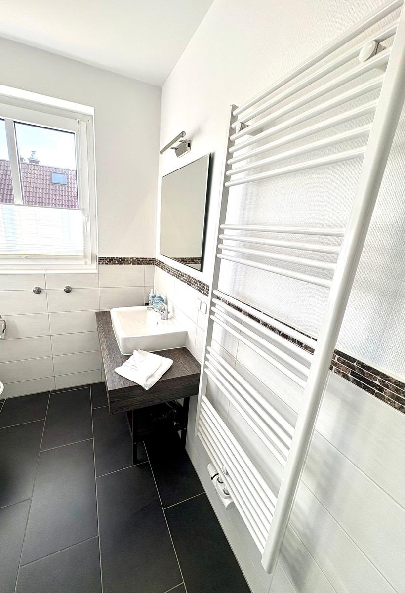 Badezimmer mit Waschbecken, Spiegel und Heizkörper an der Wand.