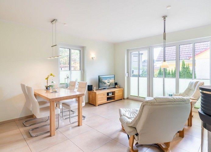 Wohn- und Essbereich mit Tisch, Stühlen, TV und Sitzgelegenheiten. Große Fensterfront mit Blick auf Garten.
