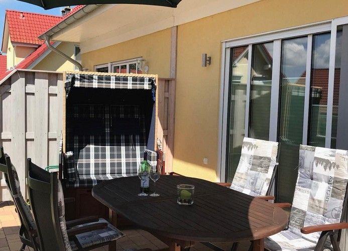 Terrasse mit Tisch, Stühlen und Schirm. Hintergrund: Haus mit Schiebetür.