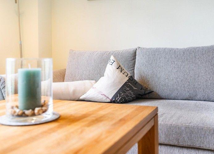 Ein grauer Sofa mit Kissen und einem Holztisch mit Kerze.