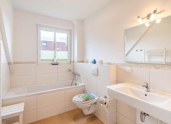 Badezimmer mit Badewanne, Toilette und Waschbecken. Fenster mit Blick auf Dach.