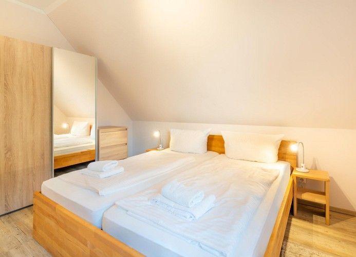 Schlafzimmer mit Doppelbett, Nachttischen und Spiegelschrank unter schrägem Dach
