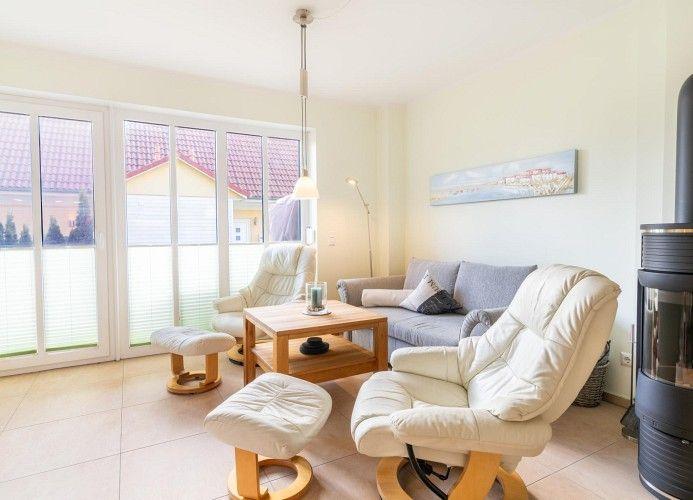 Wohnzimmer mit Sofa, zwei Sesseln und Holztisch. Durchgangstür zur Terrasse. Kaminofen.