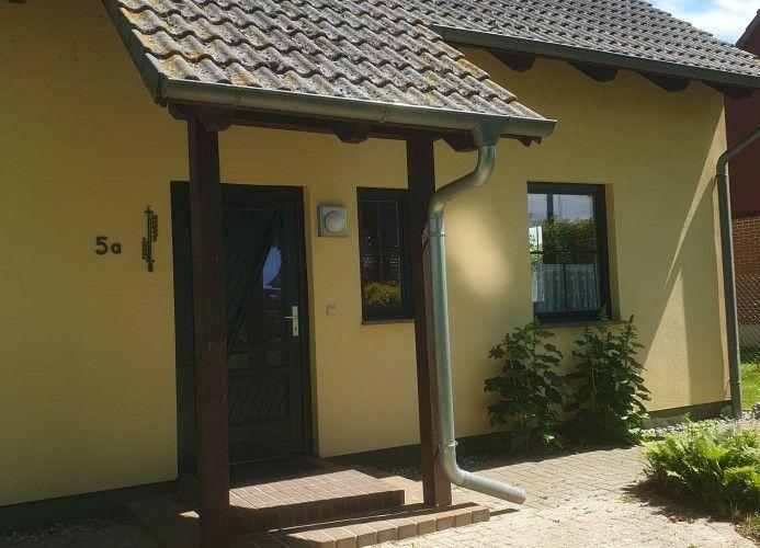 Haus mit gelber Fassade, Eingangstür und Dachüberstand. Hausnummer 5a sichtbar.