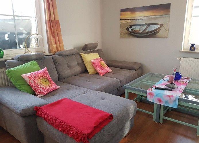 Ein Wohnzimmer mit grauem Sofa, Glas-Tisch und Wandbild mit Boot.