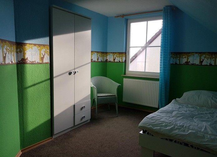 Ein Schlafzimmer mit Bett, Kleiderschrank, Stuhl und Fenster mit Vorhang.