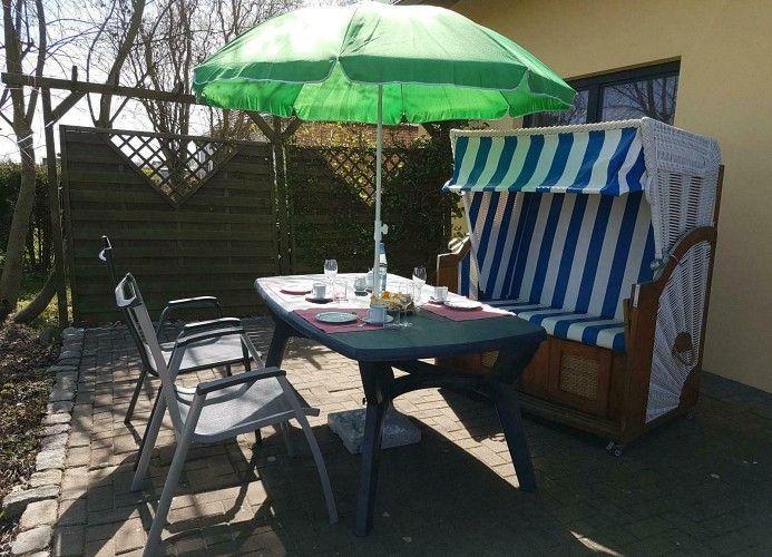 Terrasse mit Tisch, Stühlen und grünem Sonnenschirm neben Strandkorb.