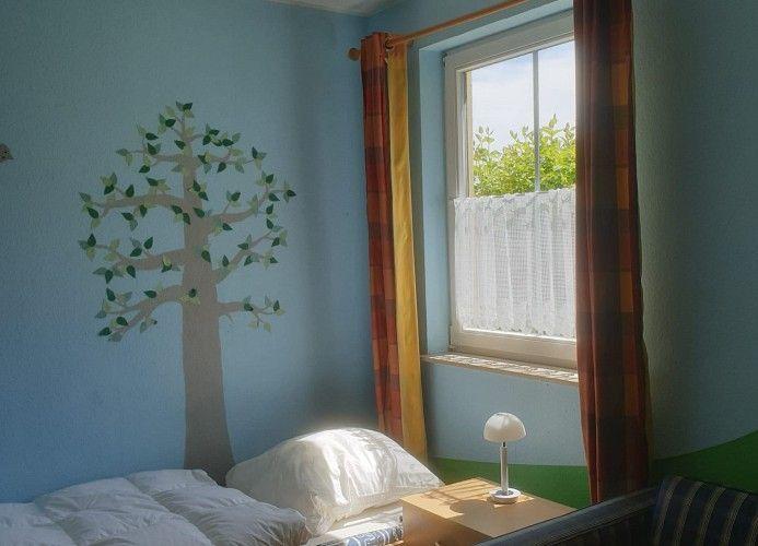 Ein Zimmer mit blauen Wänden, einem Bett und einem Fenster mit Vorhängen.