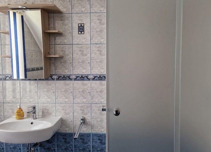 Badezimmer mit Waschbecken, Spiegel und Holzregalen an der Wand.