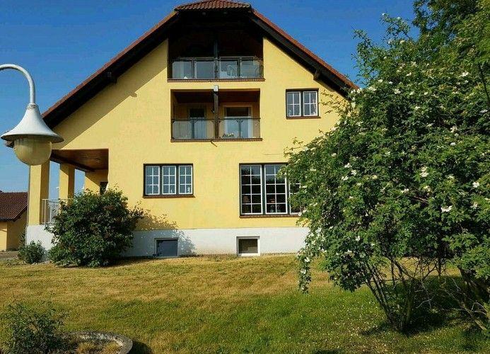 Gelbes Haus mit Balkonen und Garten. Außenbeleuchtung sichtbar.