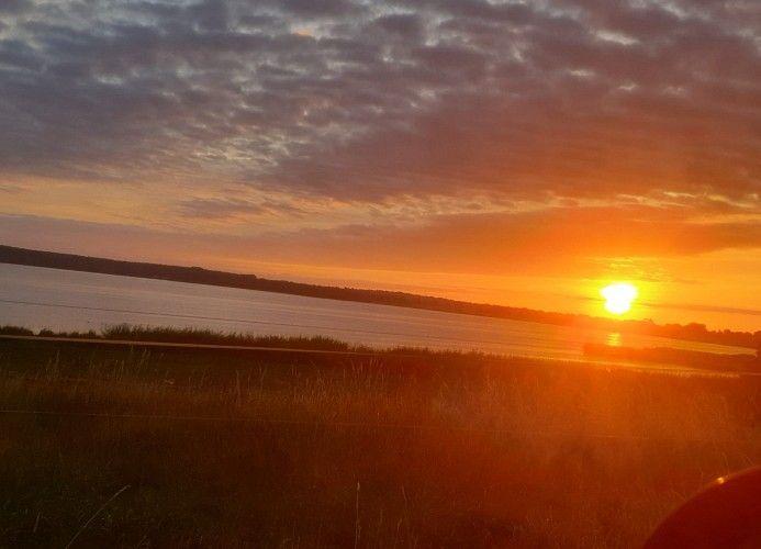 Sonnenuntergang über einem See mit bewölktem Himmel und Gras im Vordergrund.
