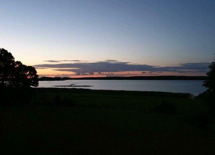 Sonnenuntergang über einem See mit Uferbereich und Bäumen im Vordergrund.