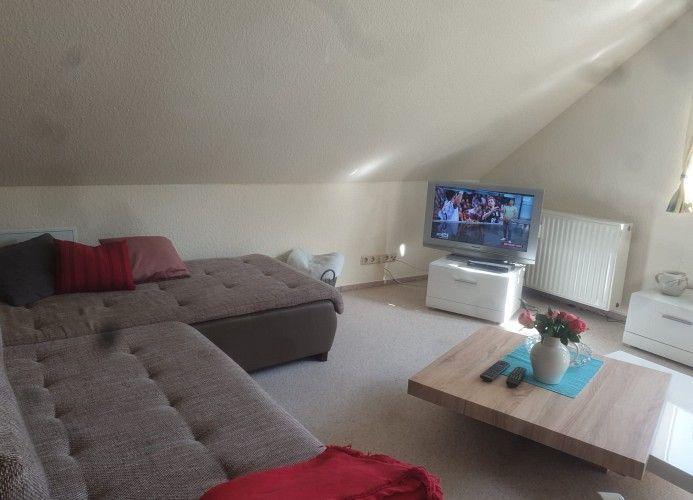 Wohnzimmer mit Schlafcouch, Fernseher und Holztisch unter schrägen Dachschrägen.