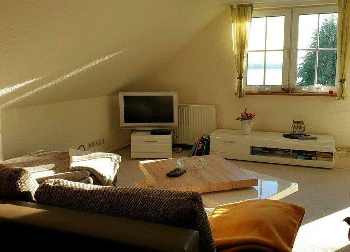 Wohnzimmer mit Fernseher, Couch und Fenster mit Blick auf Wasser.