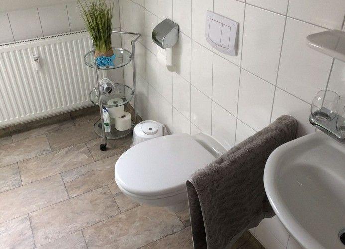 Badezimmer mit Toilette, Waschbecken und Duschbereich. Fliesenboden und weiße Wände.