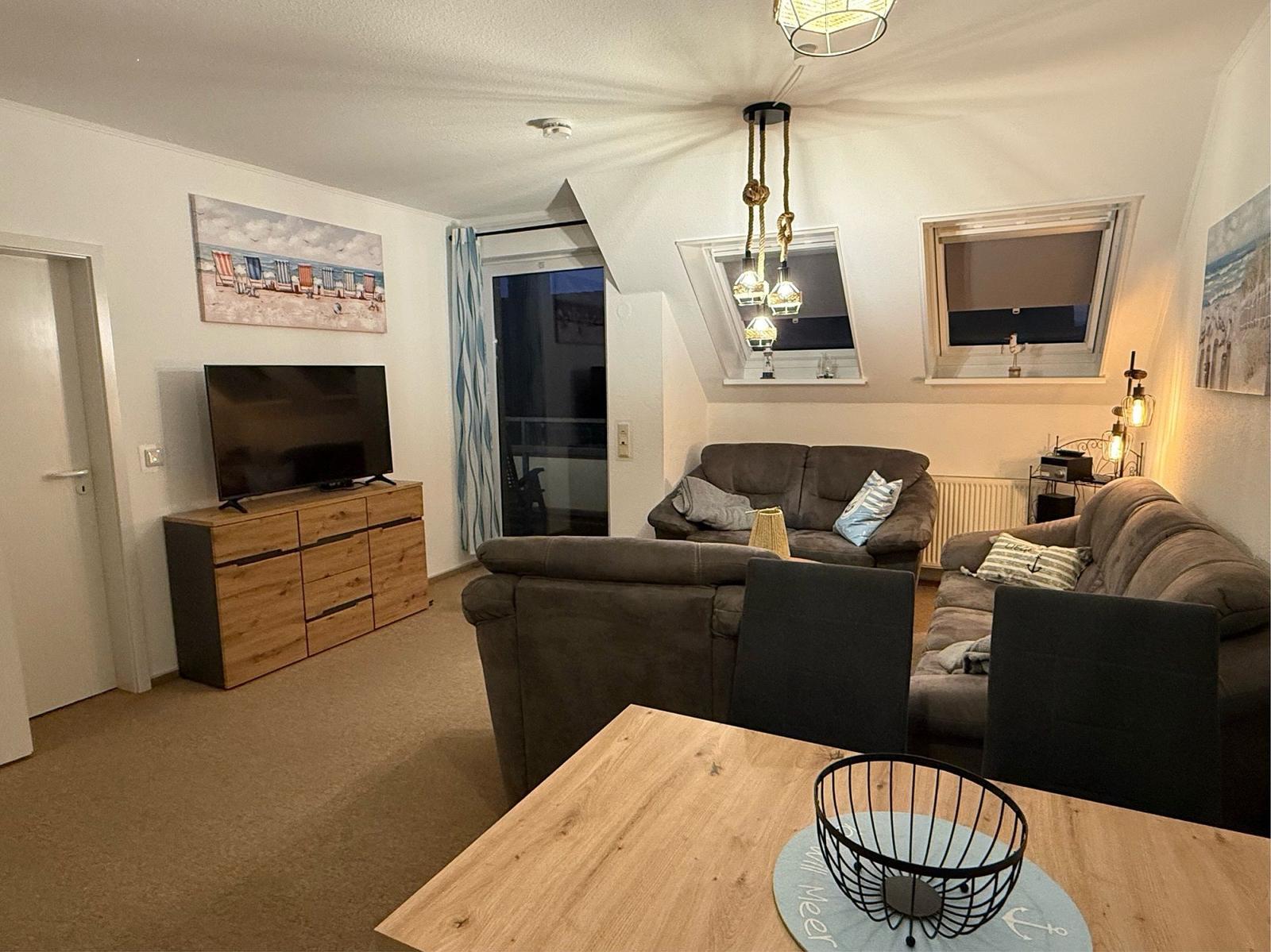 Wohnbereich mit Sofa, Fernseher und Tisch. Dachfenster und Balkontür.