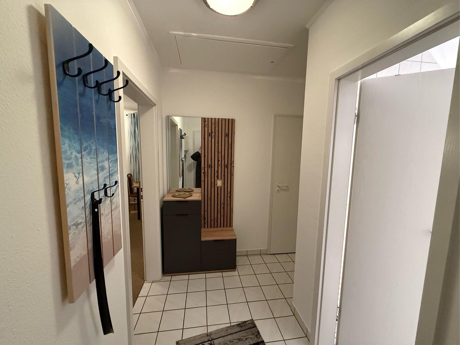 Flur mit Garderobe, Spiegel und Holzpaneelen. Weiße Wände und Fliesenboden.