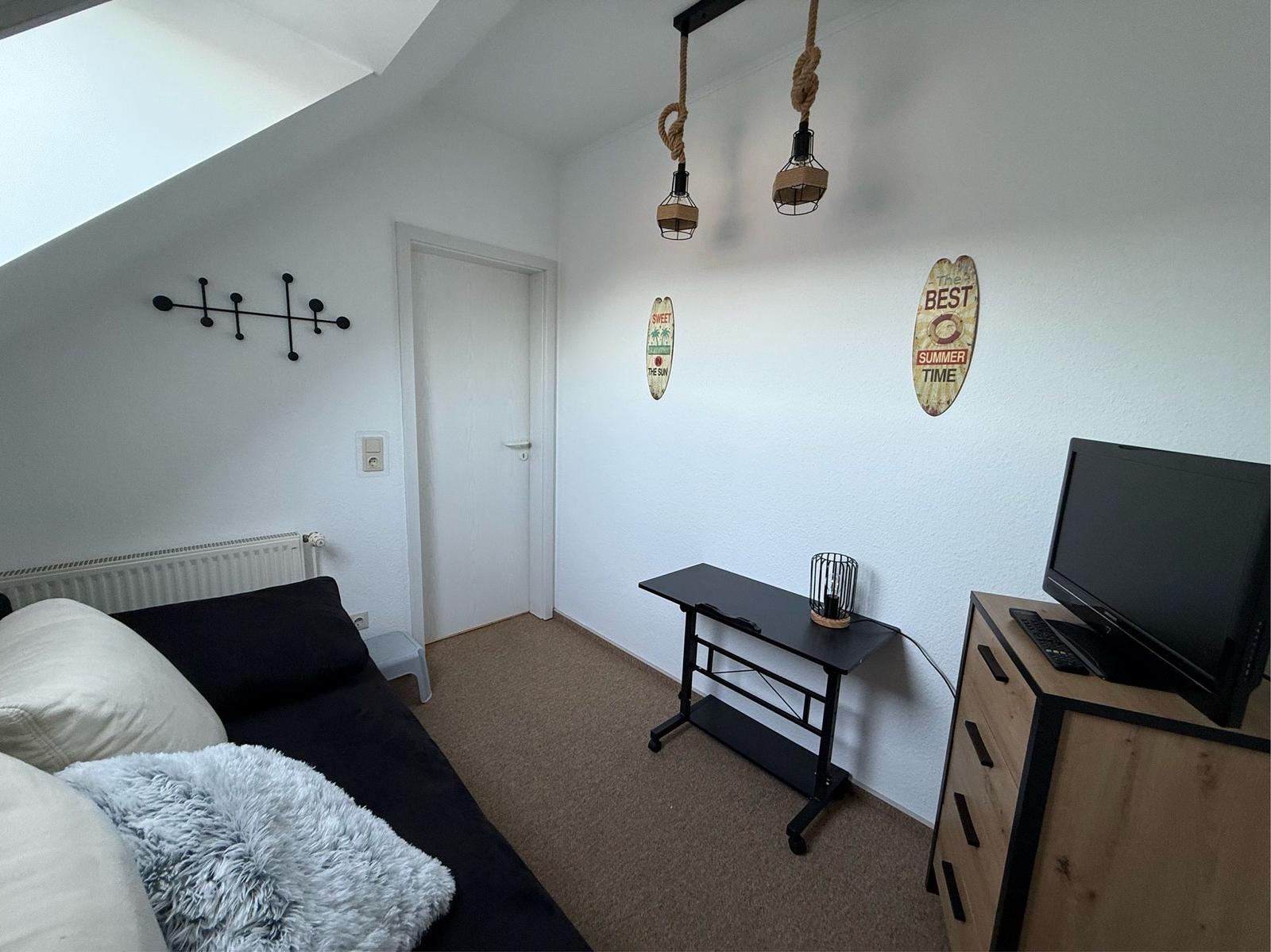 Schlafzimmer mit Dachschrägen, Bett, TV-Schrank und Hängelampen.