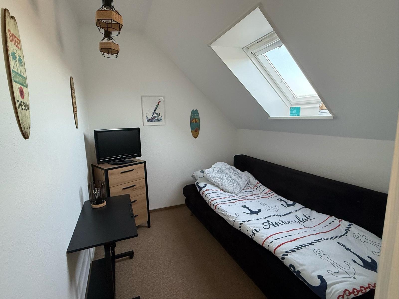 Schlafzimmer mit Dachschrägen, Dachfenster, Bett und Schreibtisch.