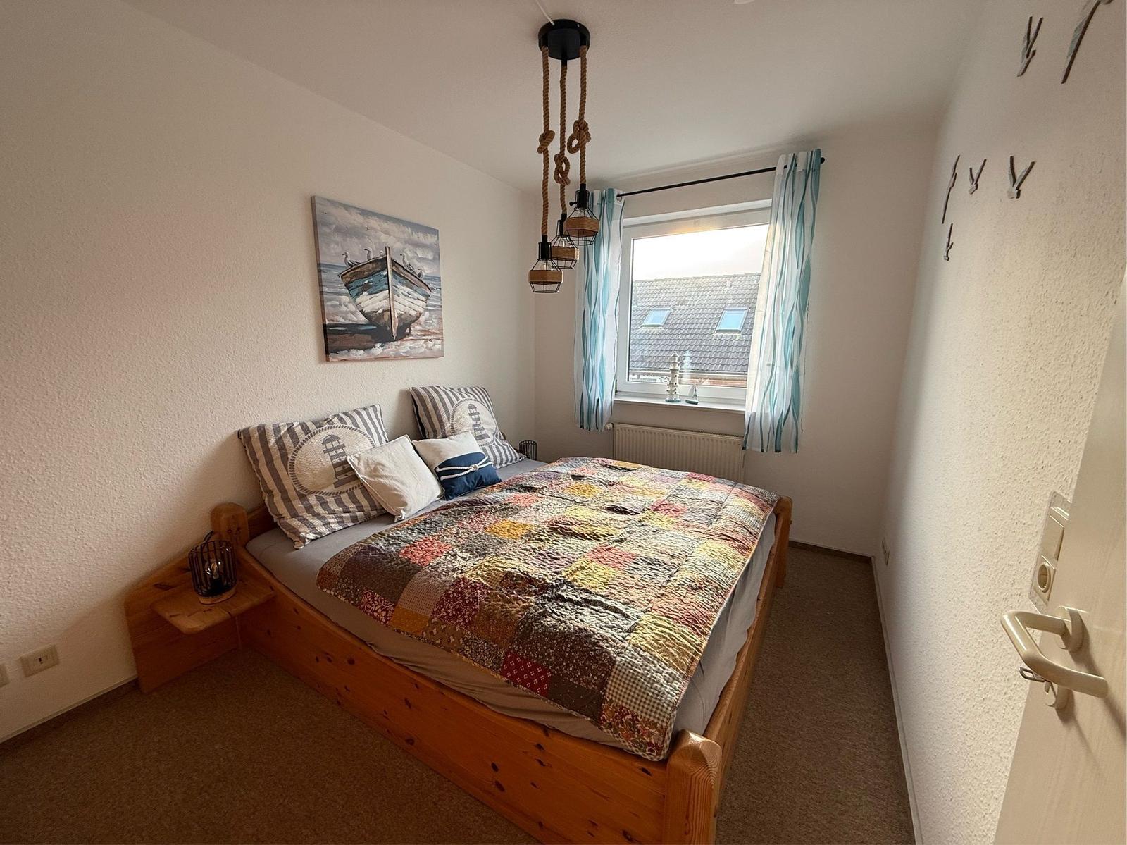 Schlafzimmer mit Holzbett, Fenster mit Vorhängen und Wandbild mit Boot.