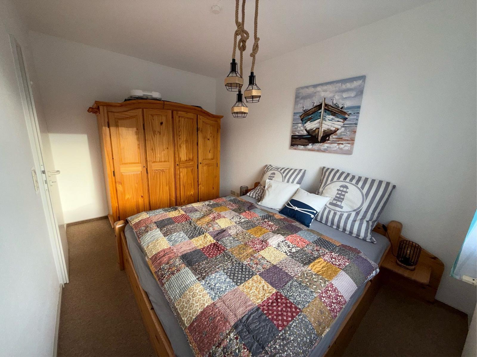 Schlafzimmer mit Holzbett, Kleiderschrank und Wandbild mit Boot.