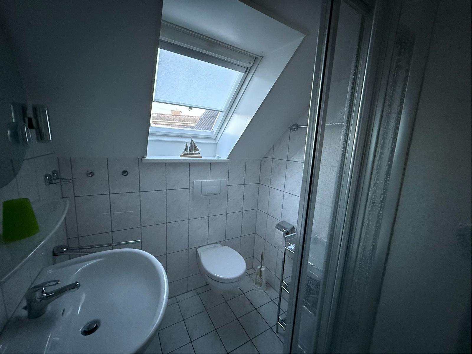 Badezimmer mit Dusche, WC und Waschbecken unter Dachschräge mit Fenster.