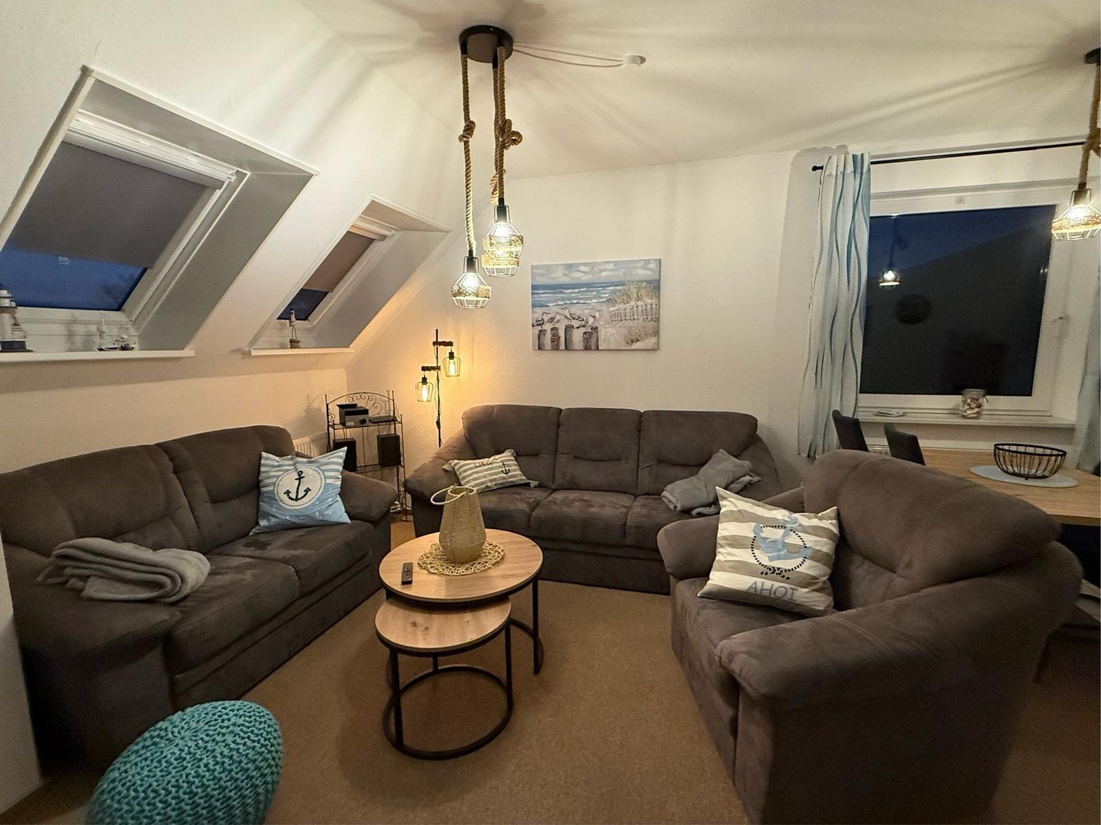 Wohnzimmer mit drei Sofas, runden Tischen und Dachfenstern. Wandbild zeigt Strand.