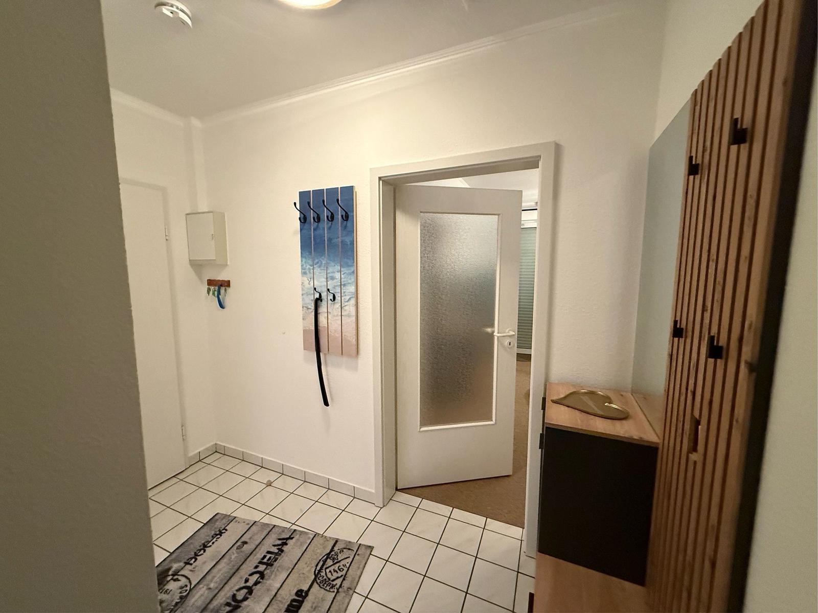 Eingangsbereich mit Fliesenboden, Holzgarderobe und Wandhaken mit Strandmotiv.