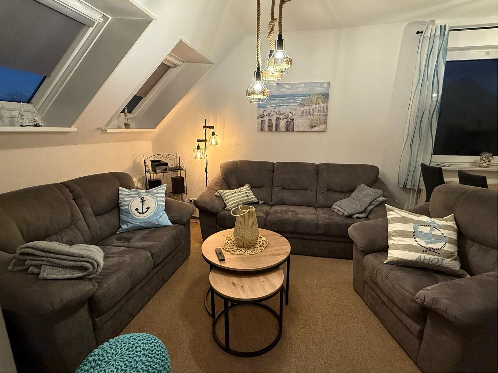 Wohnzimmer mit zwei Sofas, runden Tischen und Fenstern. Wandbild und Deckenleuchten.