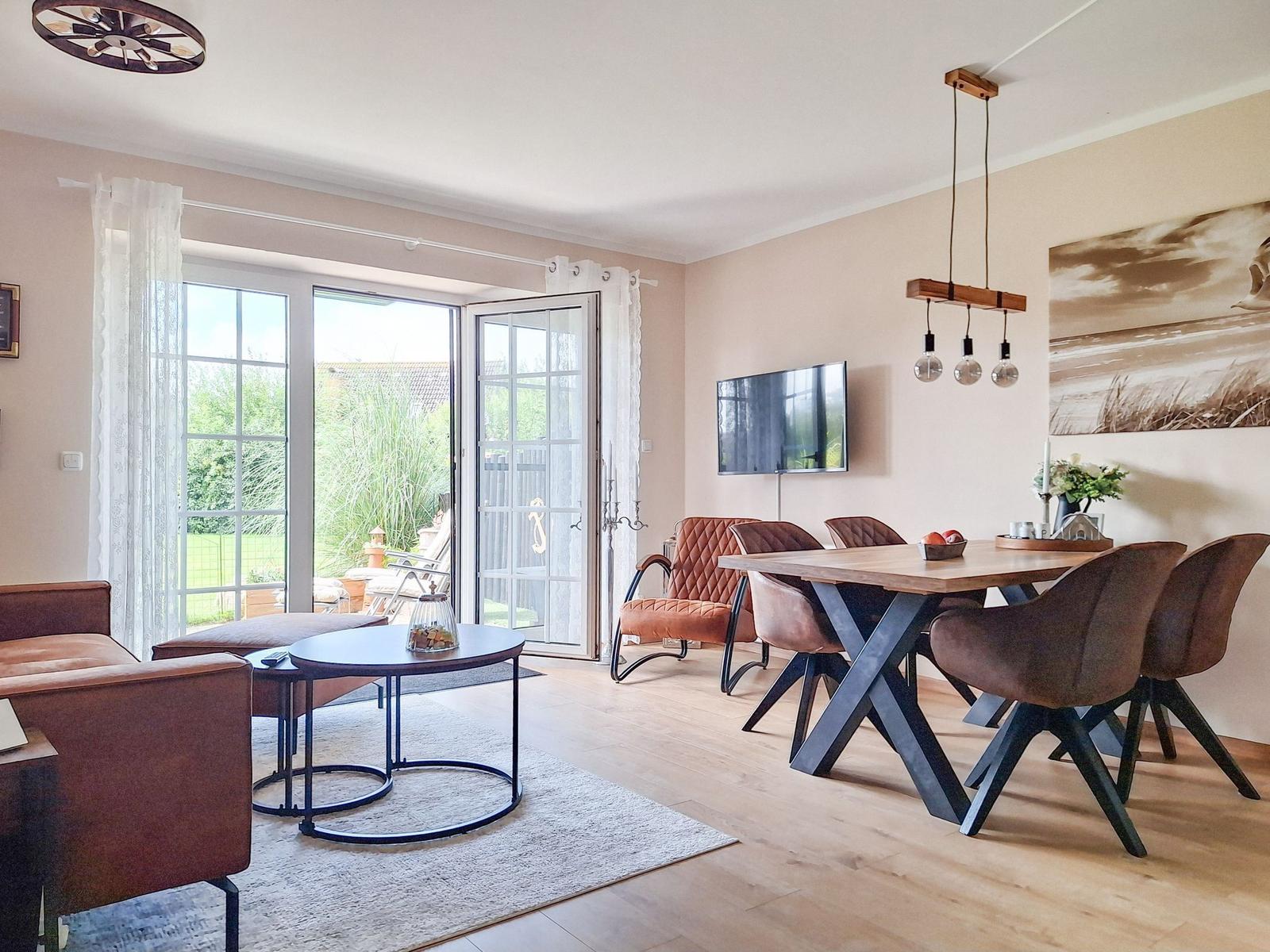 Wohn- und Essbereich mit Holzboden, Esstisch, TV und Terrassentür.