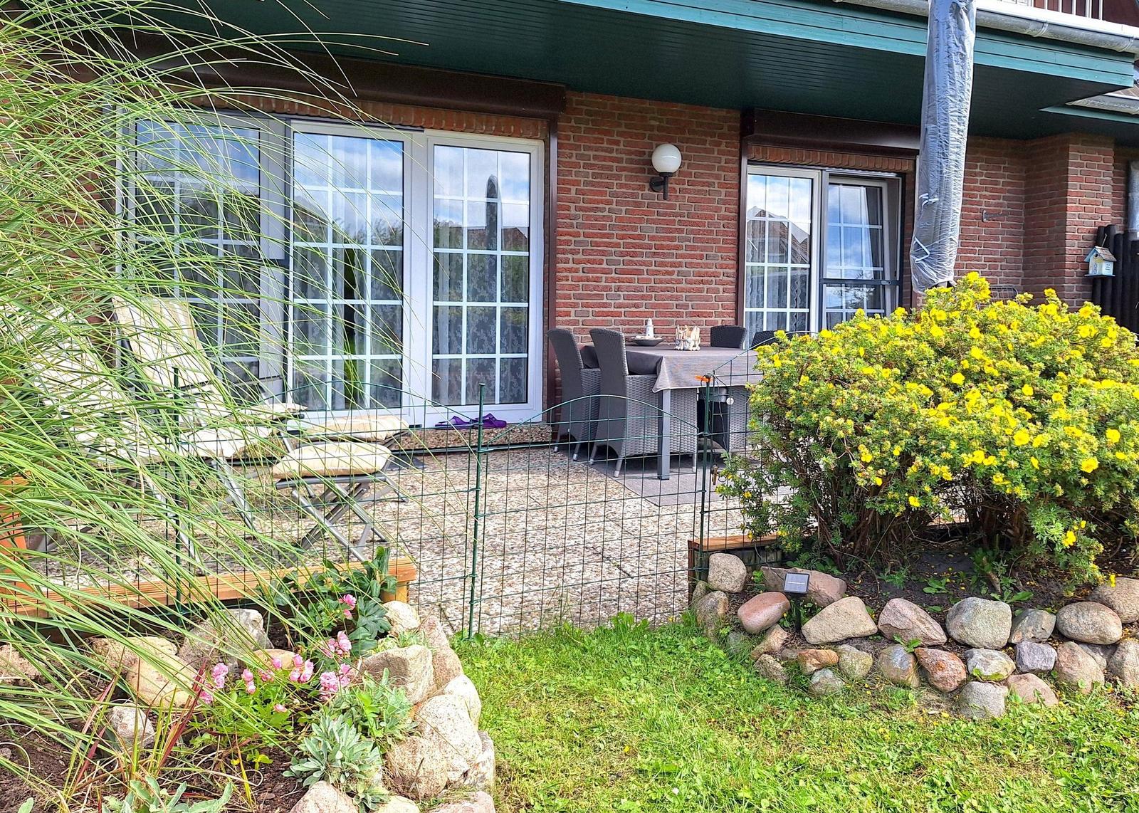 Terrasse mit Tisch und Stühlen, umgeben von Grünflächen und Blumen.