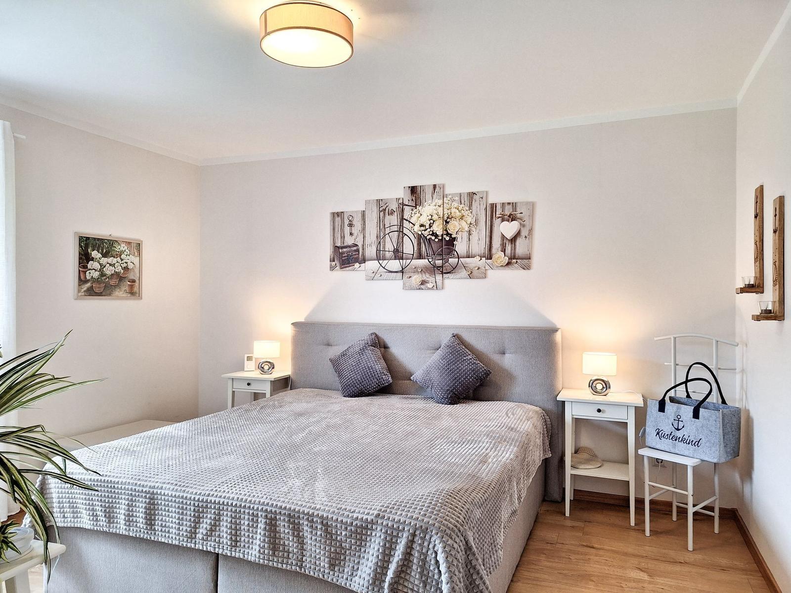 Schlafzimmer mit Bett, Nachttischen und Wandbildern.