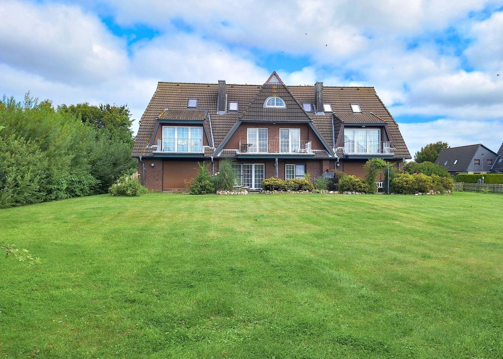 Haus mit braunem Dach und grünem Garten unter blauem Himmel.