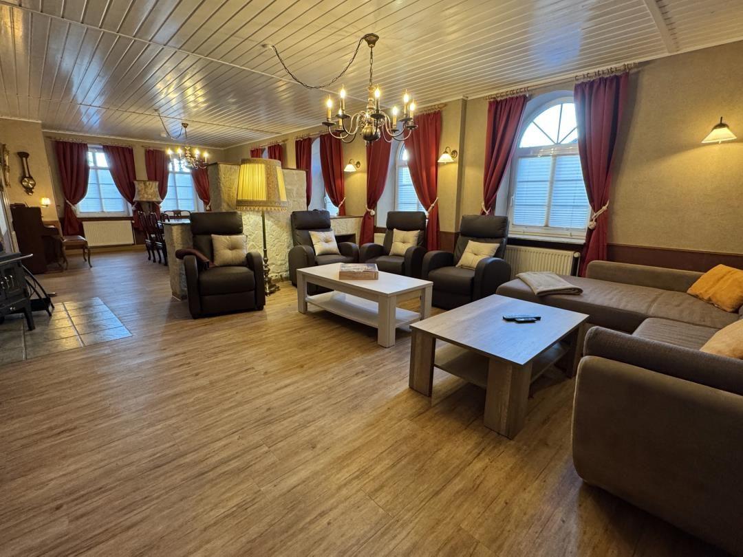 Großes Wohnzimmer mit Sitzgelegenheiten, Holzboden und Fenstern mit roten Vorhängen.