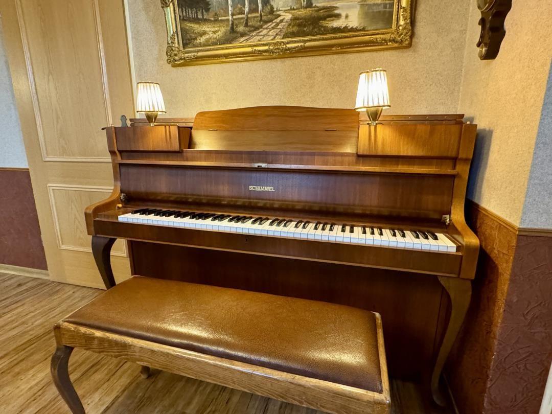 Ein Schimmel-Flügel mit Holzrahmen und Sitzbank steht in einem Raum mit Holzboden und Wandbild.