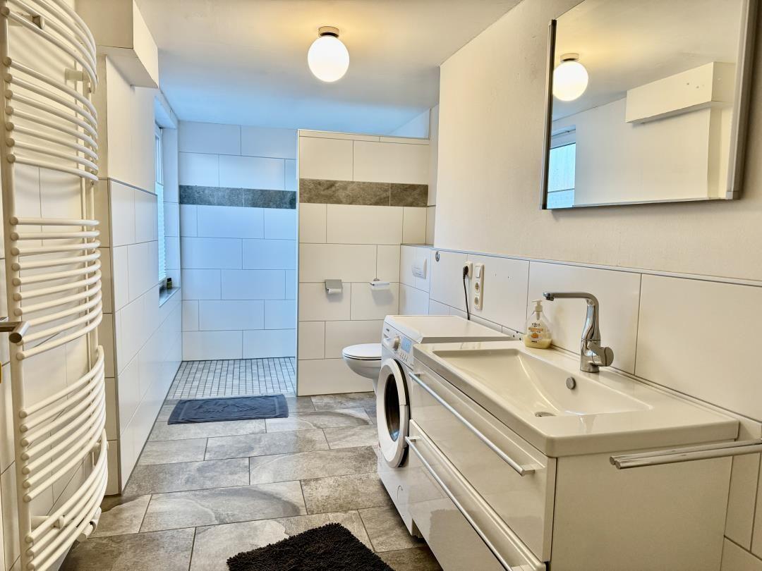 Badezimmer mit Dusche, Waschmaschine und Spiegel