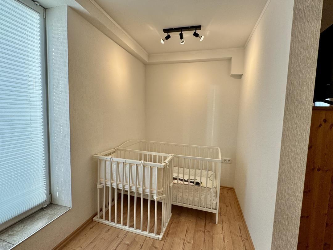 Kinderzimmer mit weißem Babybett und Holzboden. Fenster mit Jalousie.