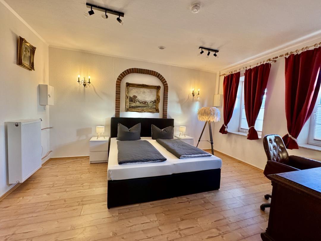 Schlafzimmer mit Doppelbett, roten Vorhängen und Holzboden.