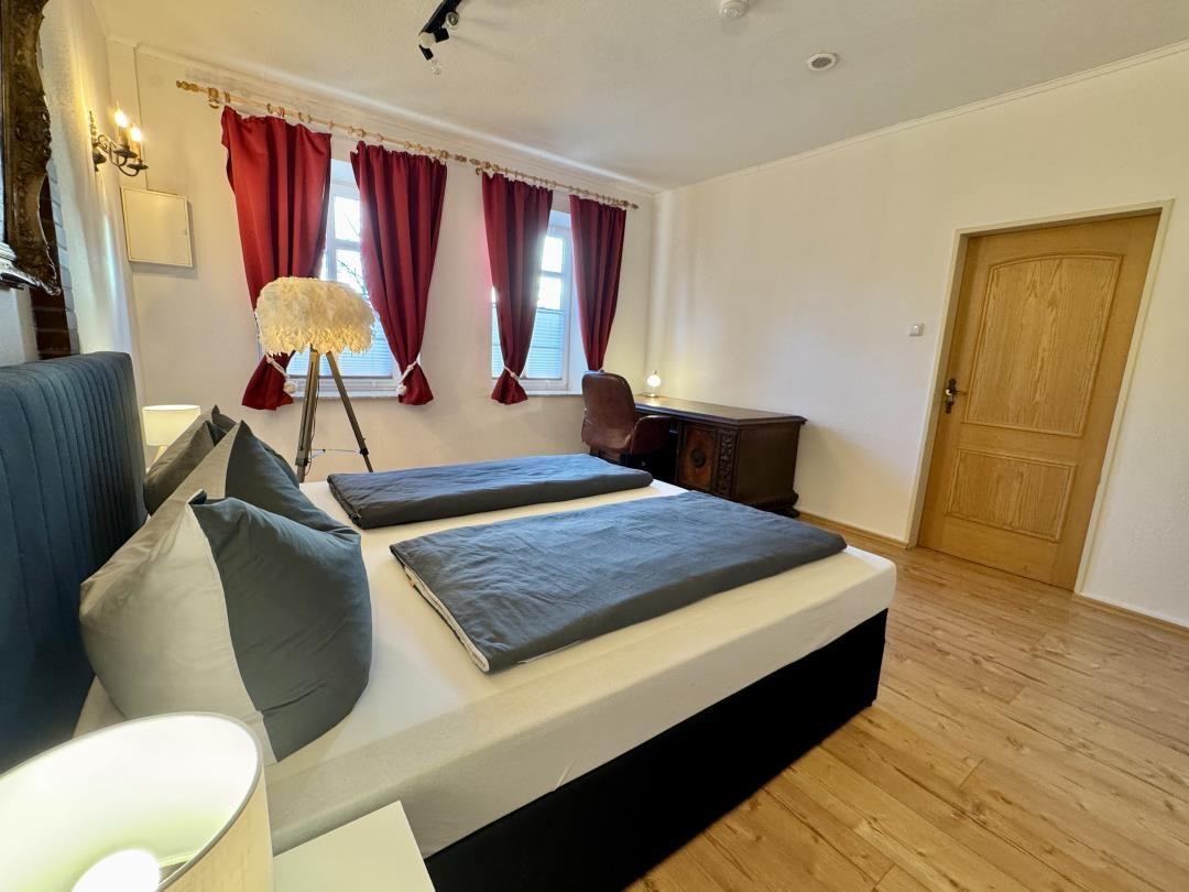 Schlafzimmer mit Doppelbett, roten Vorhängen und Holzboden.