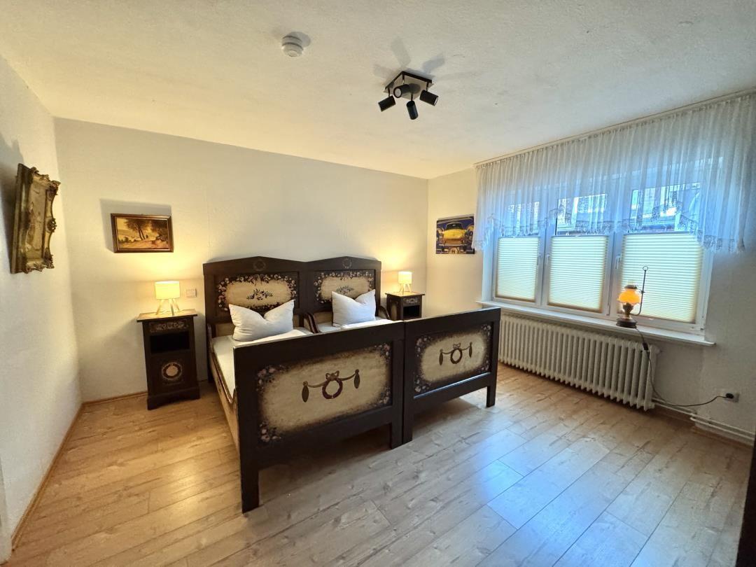 Schlafzimmer mit Doppelbett, zwei Nachttischen und Fenster mit Jalousien.